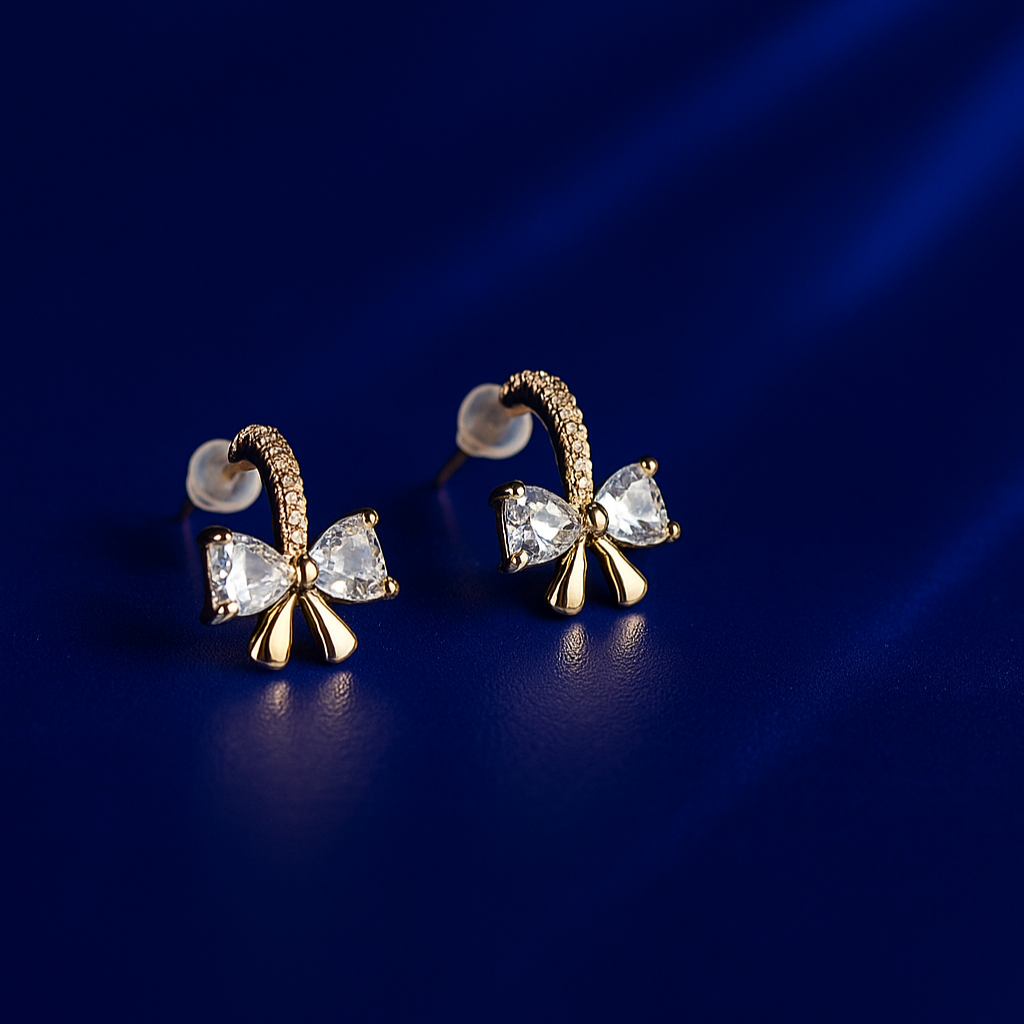 Gold bow-shaped earrings with clear gemstones on a dark blue background